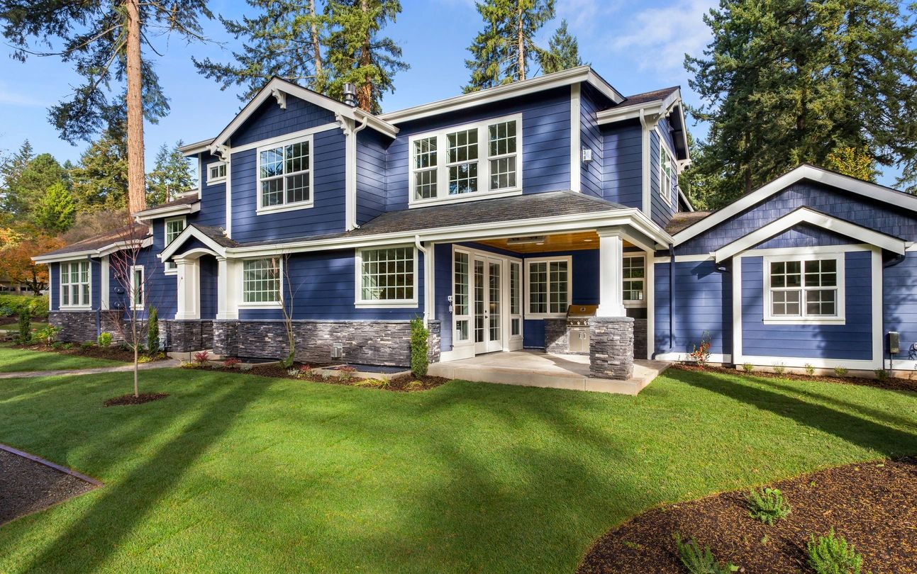 Facade of home with manicured lawn, and backdrop of trees and blue sky